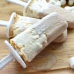 closeup of 3 S'mores Popsicles arranged decoratively amongst mini marshmallows on board.