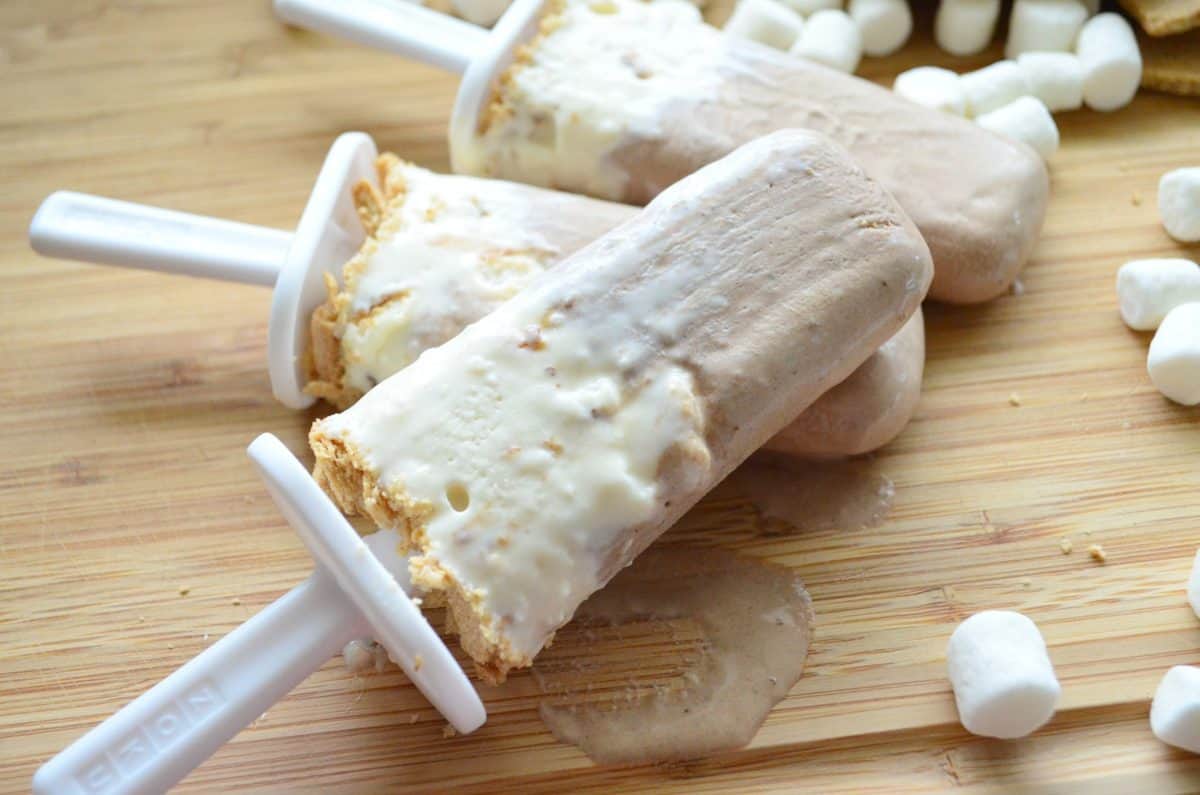 3 light brown and white popsicles on countertop with mini marshmallows.