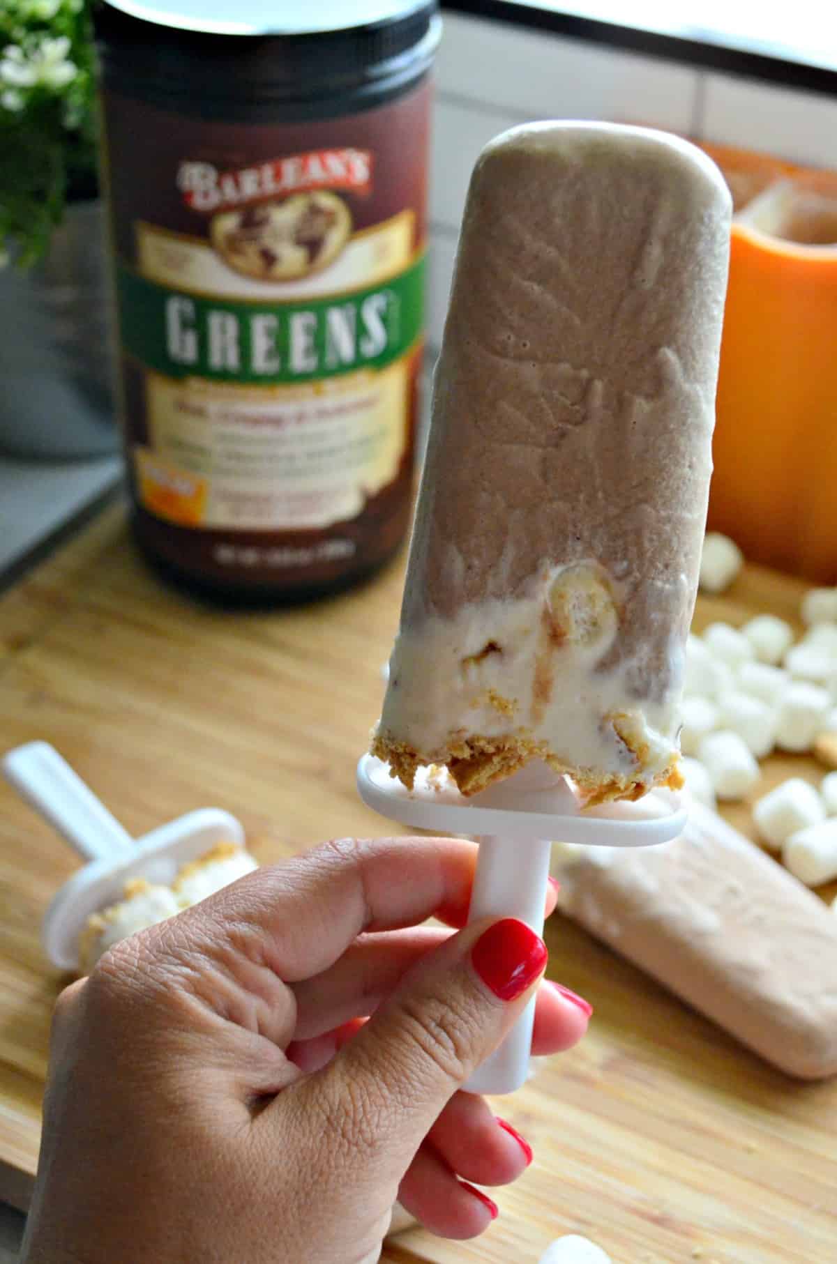 hand holding up  light brown and white popsicles over mini marshmallows and more popsicles.