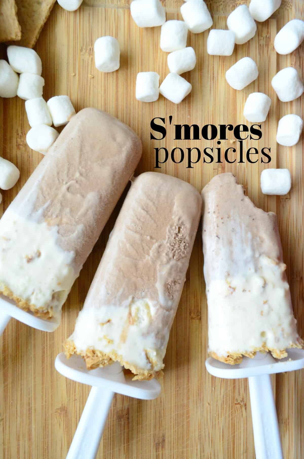 3 light brown and white popsicles on countertop with mini marshmallows and graham crackers with title text.