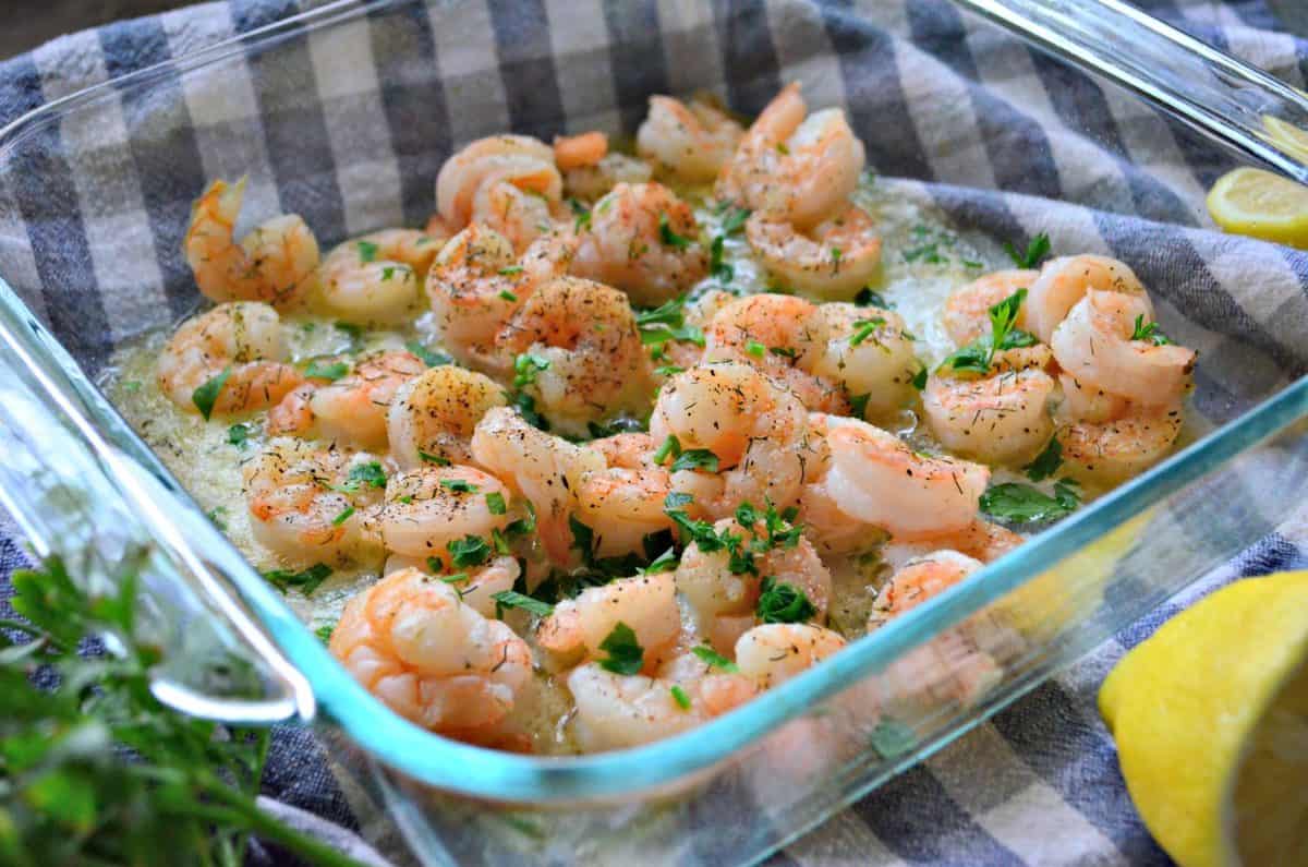 baked lemon garlic shrimp in melted butter in glass dish topped with herbs and spices.