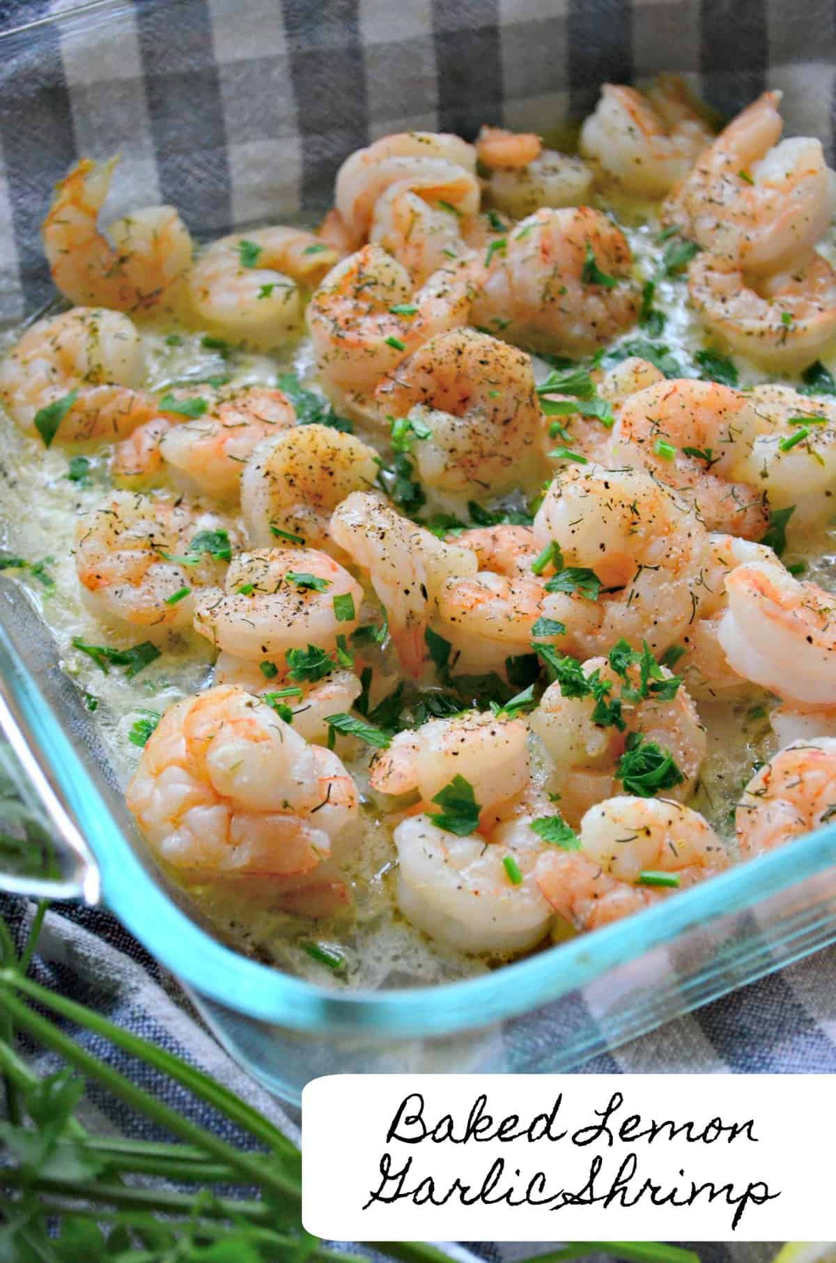 baked lemon garlic shrimp in melted butter in glass dish topped with herbs and spices with title text.