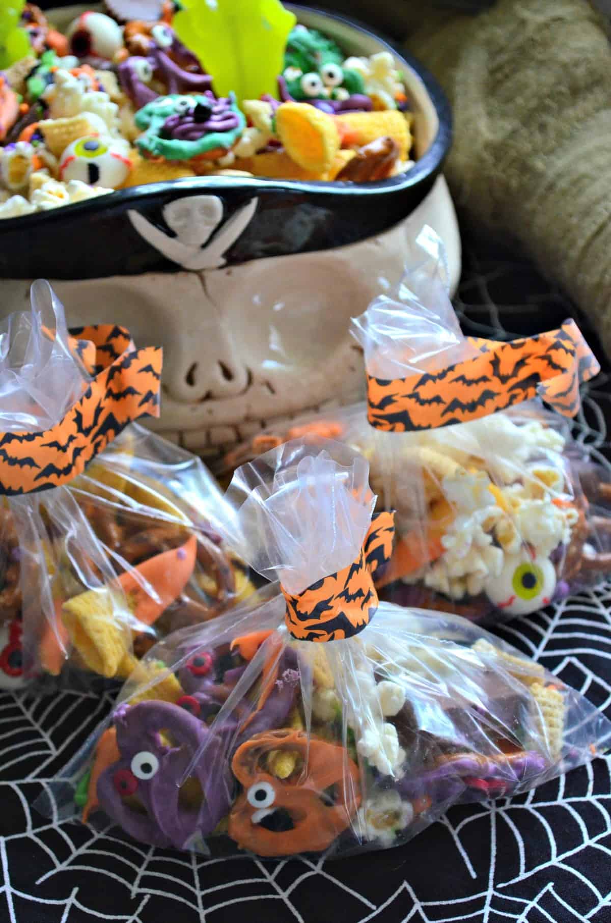 baggies of  snack mix with colorful chocolate dipped pretzels and candy eyes with bowl of snack mix behind.