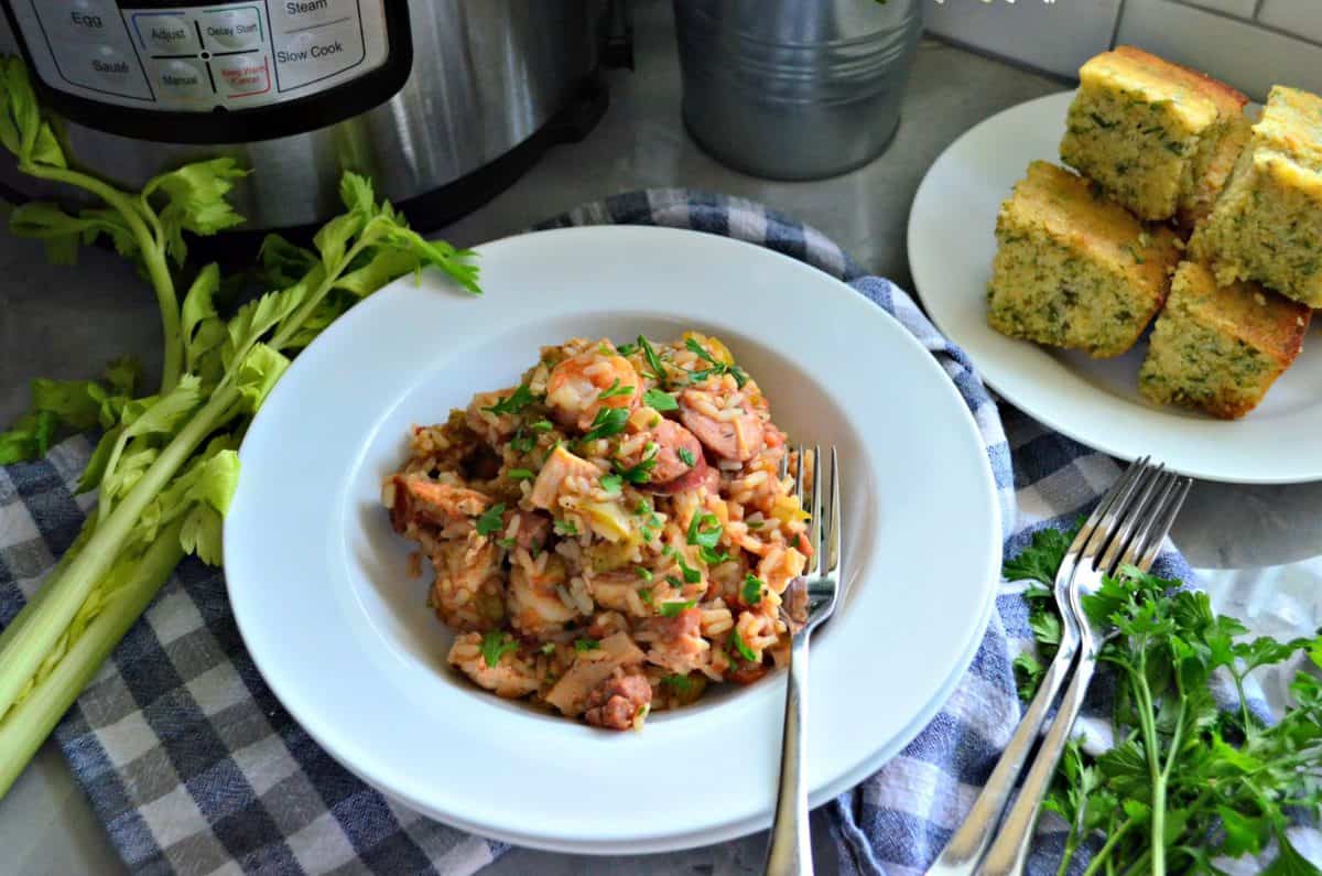 Chicken, Andouille Sausage, and Shrimp Jambalaya in a bowl with rice on tablecloth next to forks and corn bread.