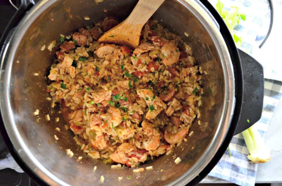 top view of Chicken, Andouille Sausage, and Shrimp with rice in an instant pot with wooden spoon.