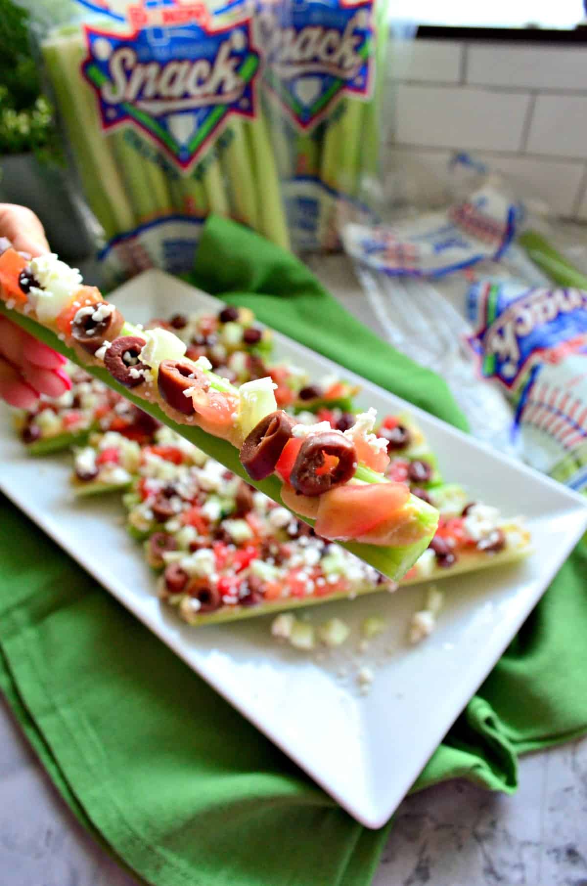 Female hand holding a stick of celery with toppings.