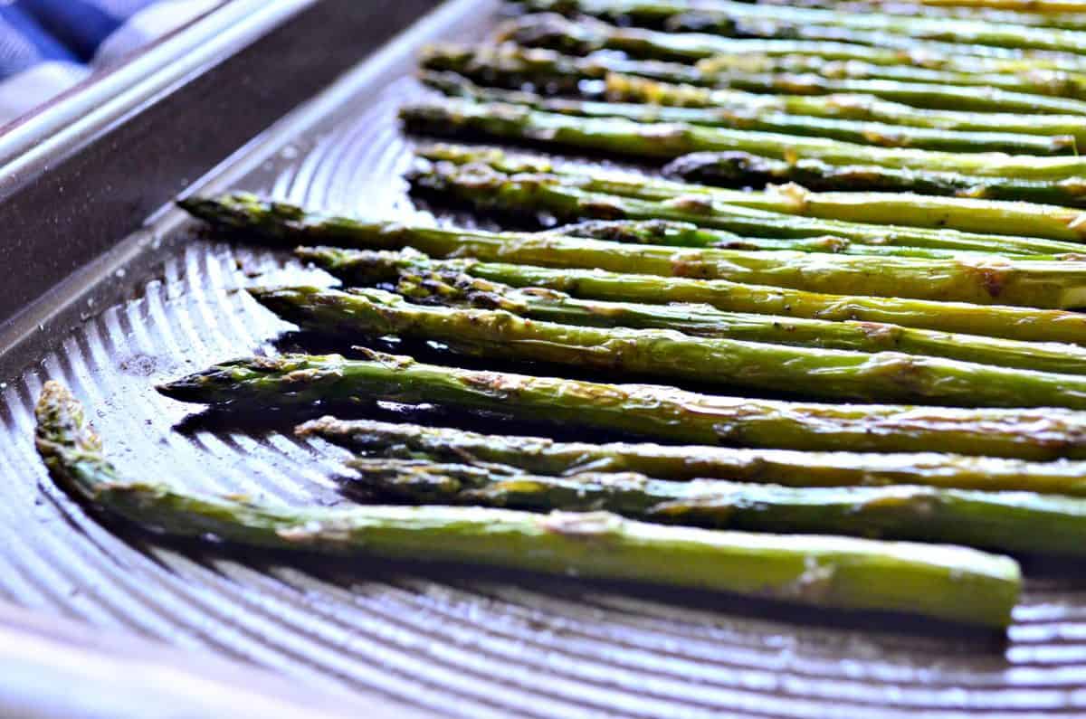 side view of roasted asparagus on sheet pan sprinkled with salt.