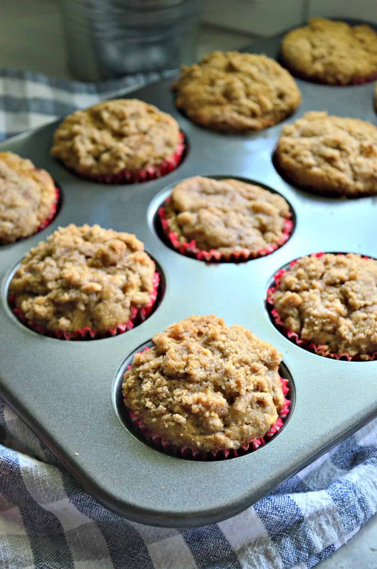 Apple Cinnamon Streusel Muffins in tin muffin pan with one in focus and the rest blurred.