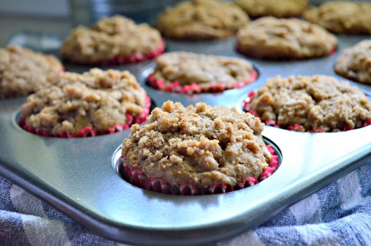 closeup of apple cinnamon streusel muffins in red papers in tin muffin pan.