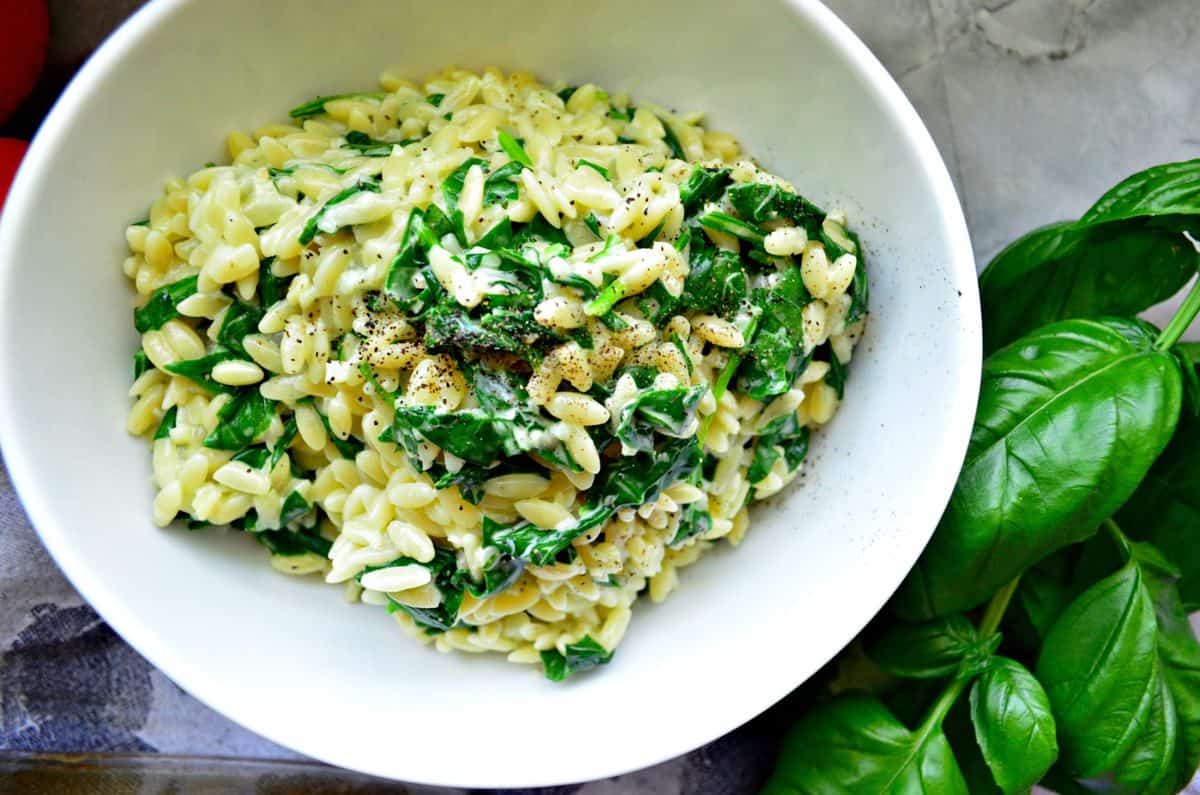 Top view Creamy Parmesan Orzo with Spinach in bowl next to basil.
