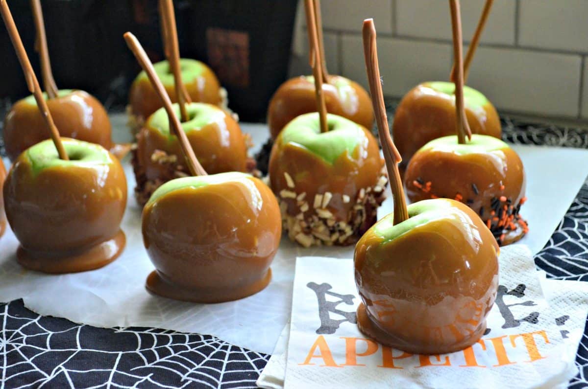 10 green apples dipped in caramel, 3 of which are covered in nuts on spiderweb platter.