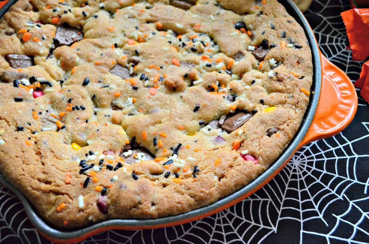 top view of a cookie with sprinkles and reeses pieces baked into a skillet on spiderweb tablecloth.