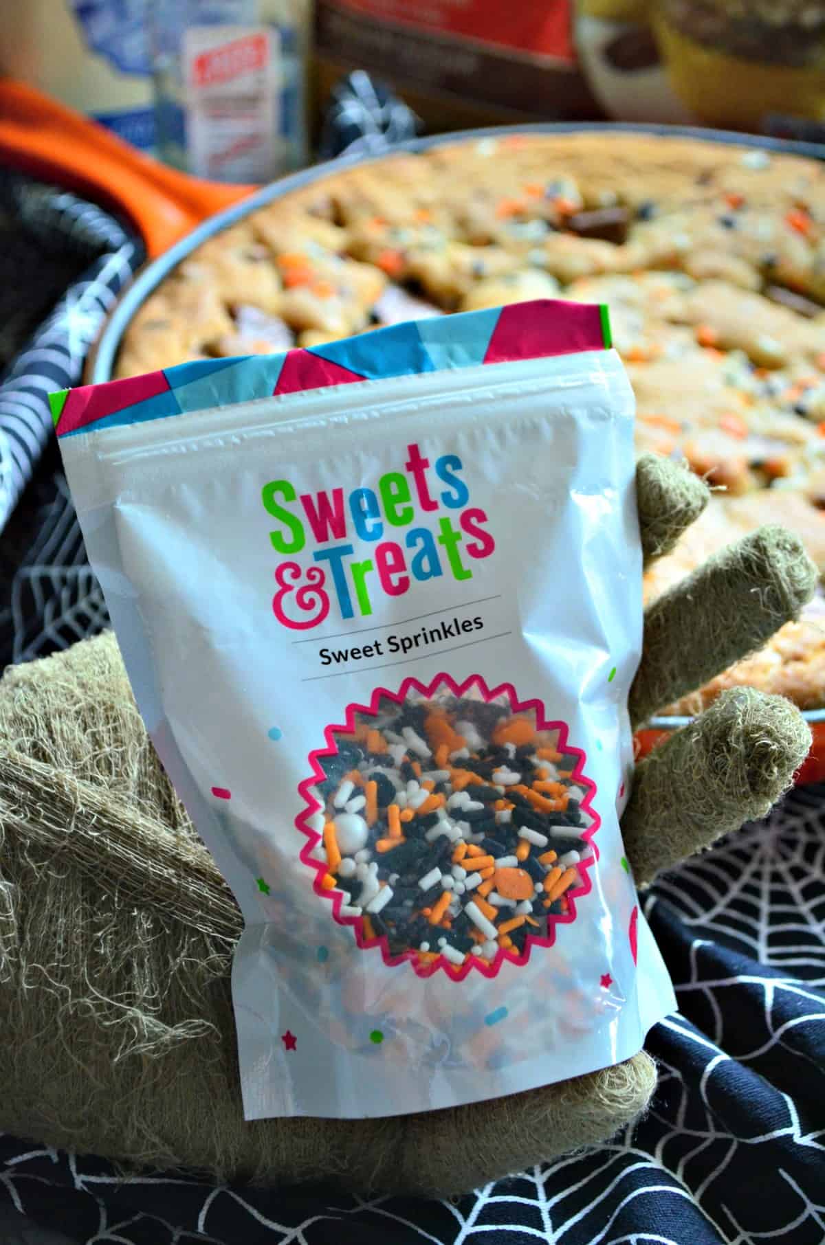 Closeup bag of Sweets & Treats Sprinkles with cookie in background.