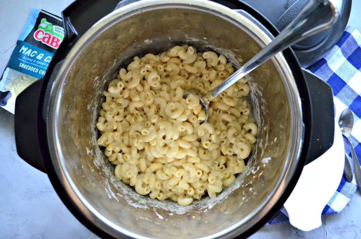 top view of white macaroni and cheese being stirred with long metal spoon in instant pot.