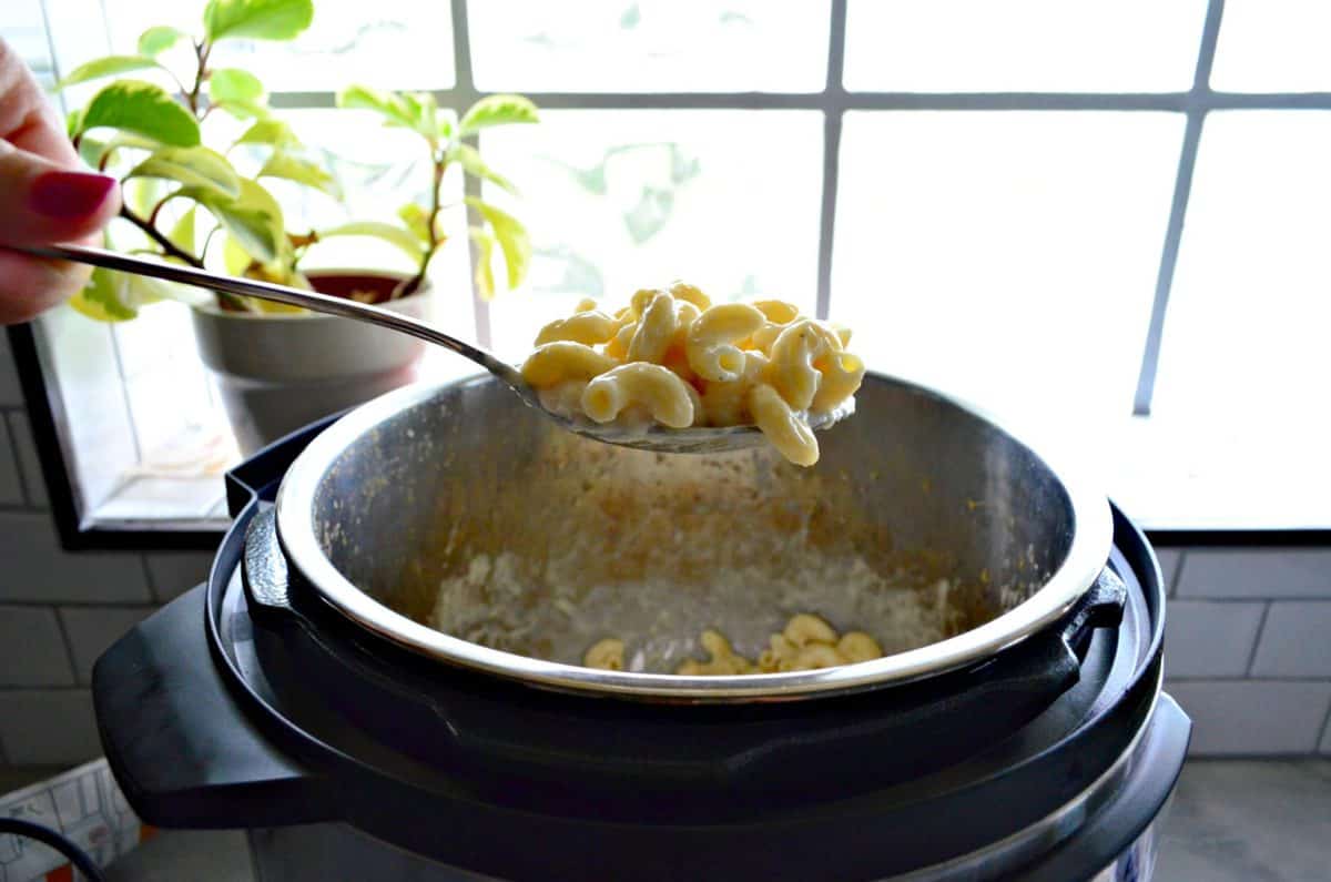 side view of spoonful of macaroni and cheese held over instant pot in front of window.