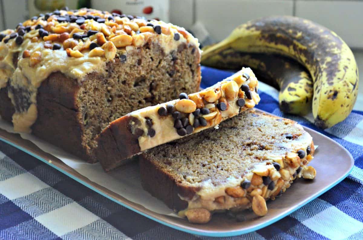 closeup of banana bread smothered in light brown mixture topped with nuts and chocolate chips near bananas.