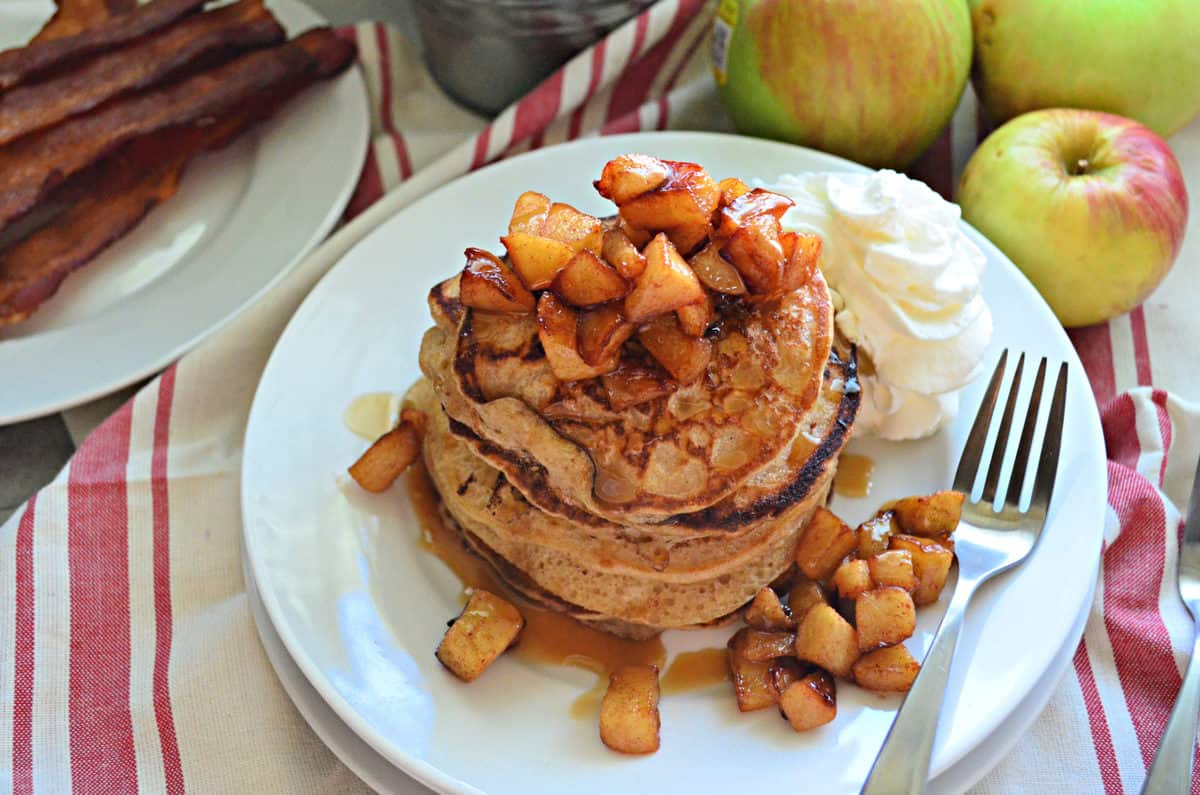 top view stack of cinnamon pancakes topped with cubed apples and syrup with whipped cream.