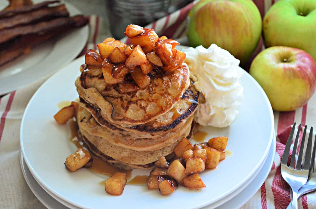 stack of cinnamon pancakes topped with cubed apples and syrup with whipped cream.