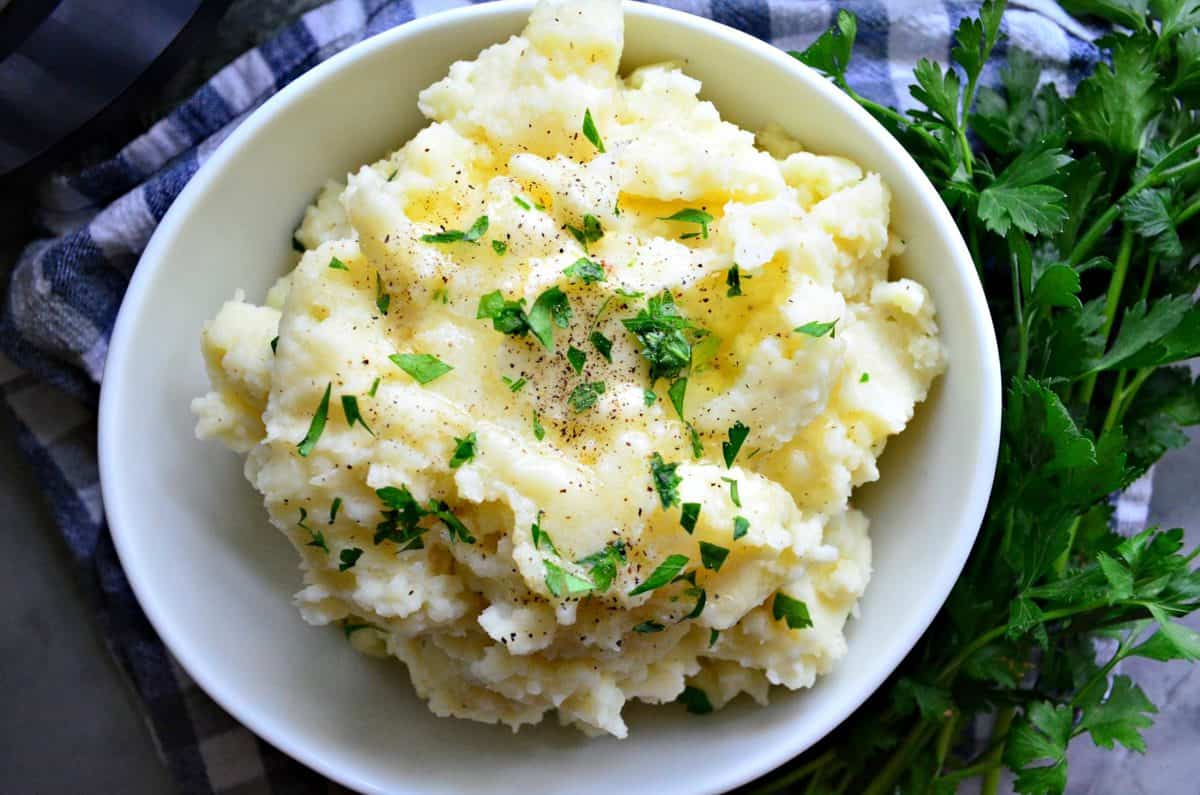 top view bowl of mashed potatoes topped with melted butter, pepper, and parsley next to parsley.