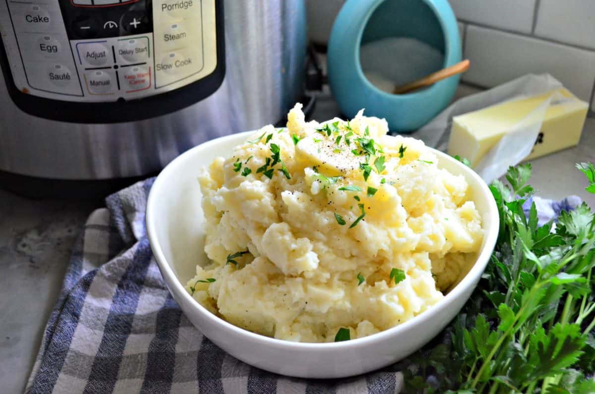 bowl of mashed potatoes topped with melted butter, pepper, and parsley in front of instant pot.