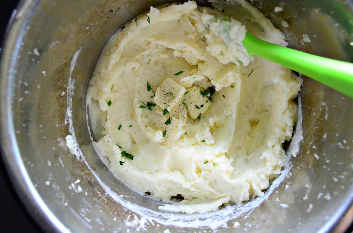 top view of mashed potatoes in instant pot with butter, herbs, and pepper being stirred in.