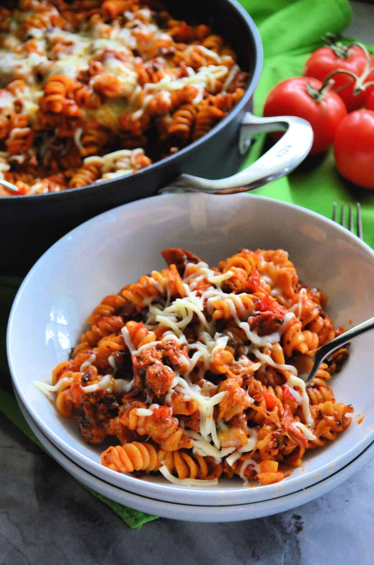 skillet and plate both with rotini in red sauce topped with herbs and melted white cheese.