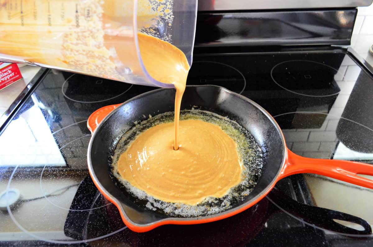 Light orange mixture being poured from measuring cup into skillet on stovetop.
