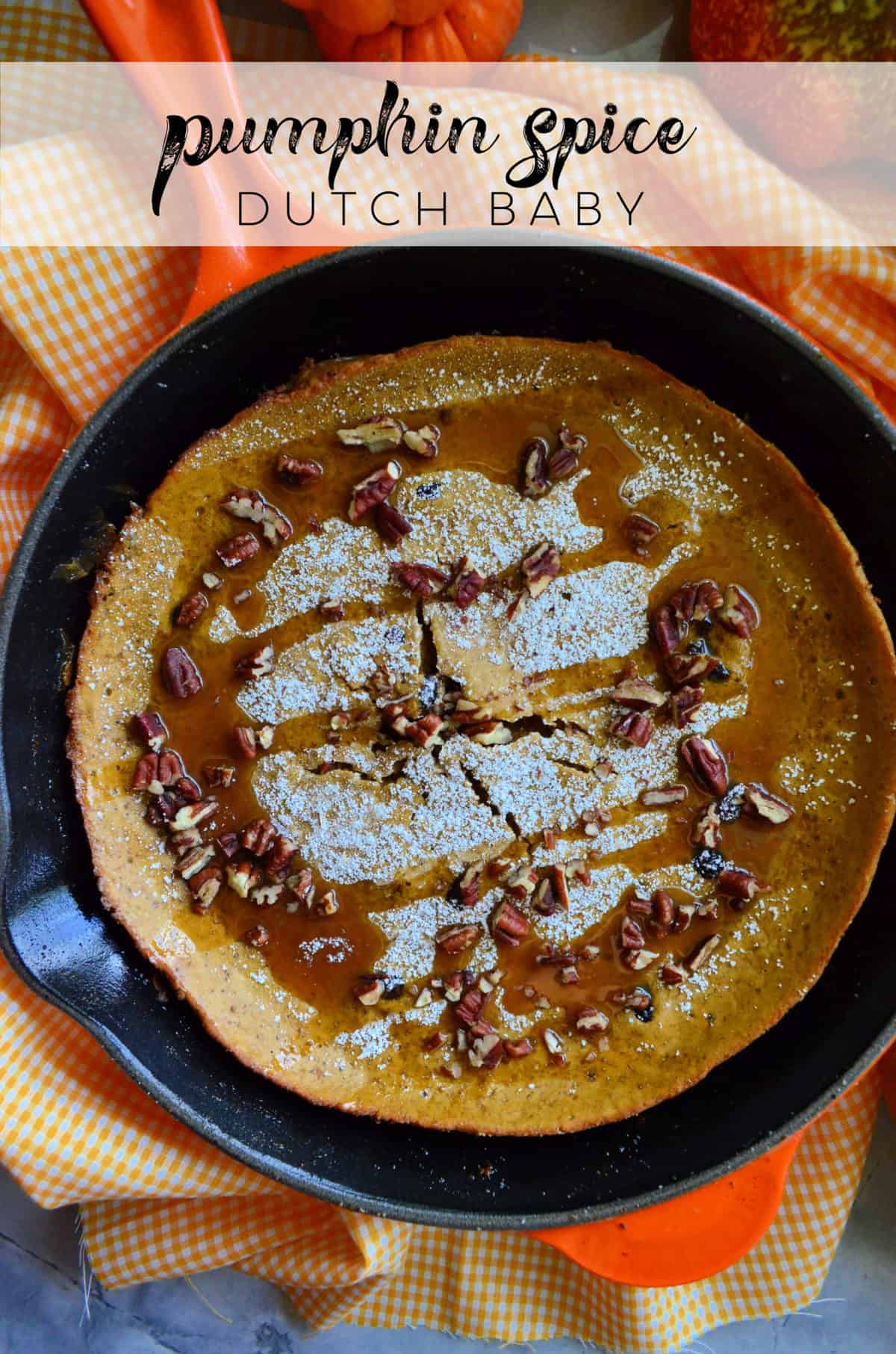 Top view of speckled brown pancake pastry in skillet topped with powdered sugar, pecans, and caramel.