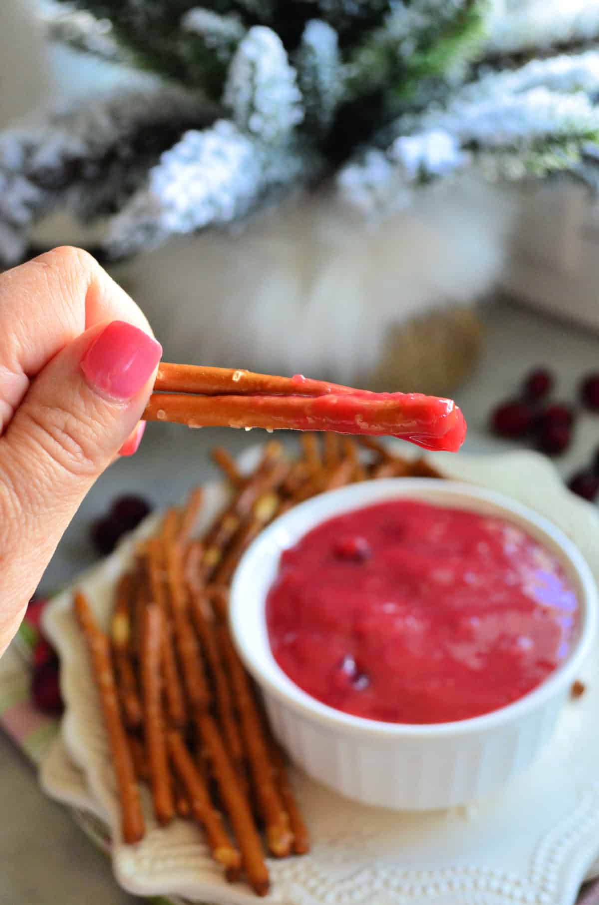 closeup hand holding up two pretzels with pink dip over dip bowl.