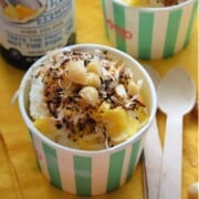 Closeup of frozen treat in paper cup topped with macadamia nuts, coconut shavings, and pineapple.