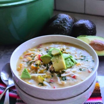 Bowl of green enchilada chicken soup stacked on top of empty bowl on colorful tablecloth with spoons.