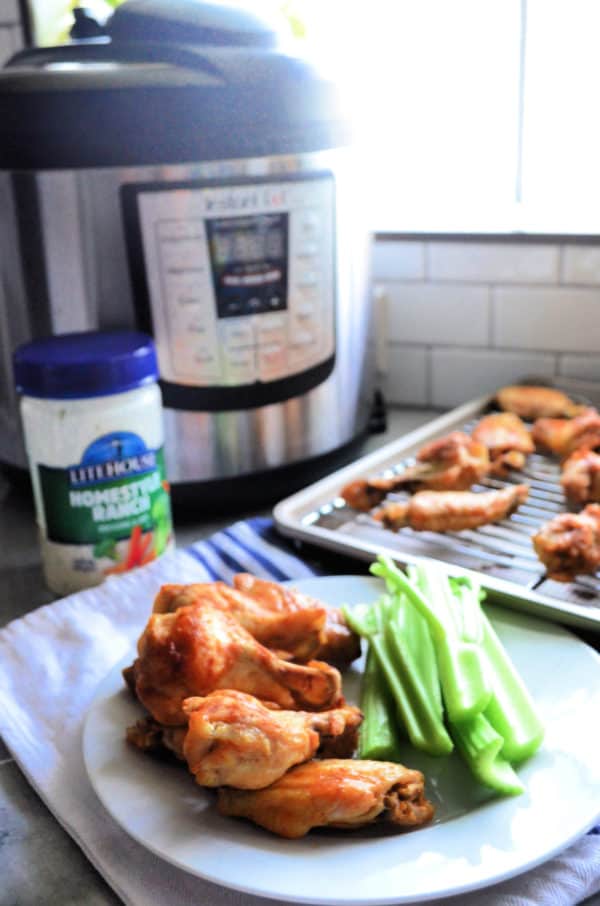 stack of chicken wings on plate with celery in front of instant pot.