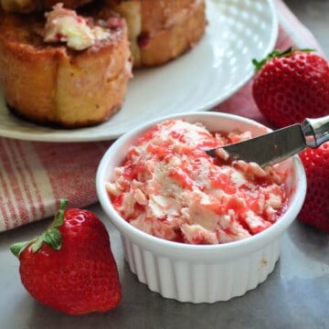 closeup of small bowl with strawberry butter and spreader next to fresh strawberries.