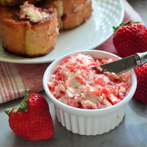 closeup of small bowl with strawberry butter and spreader next to fresh strawberries.