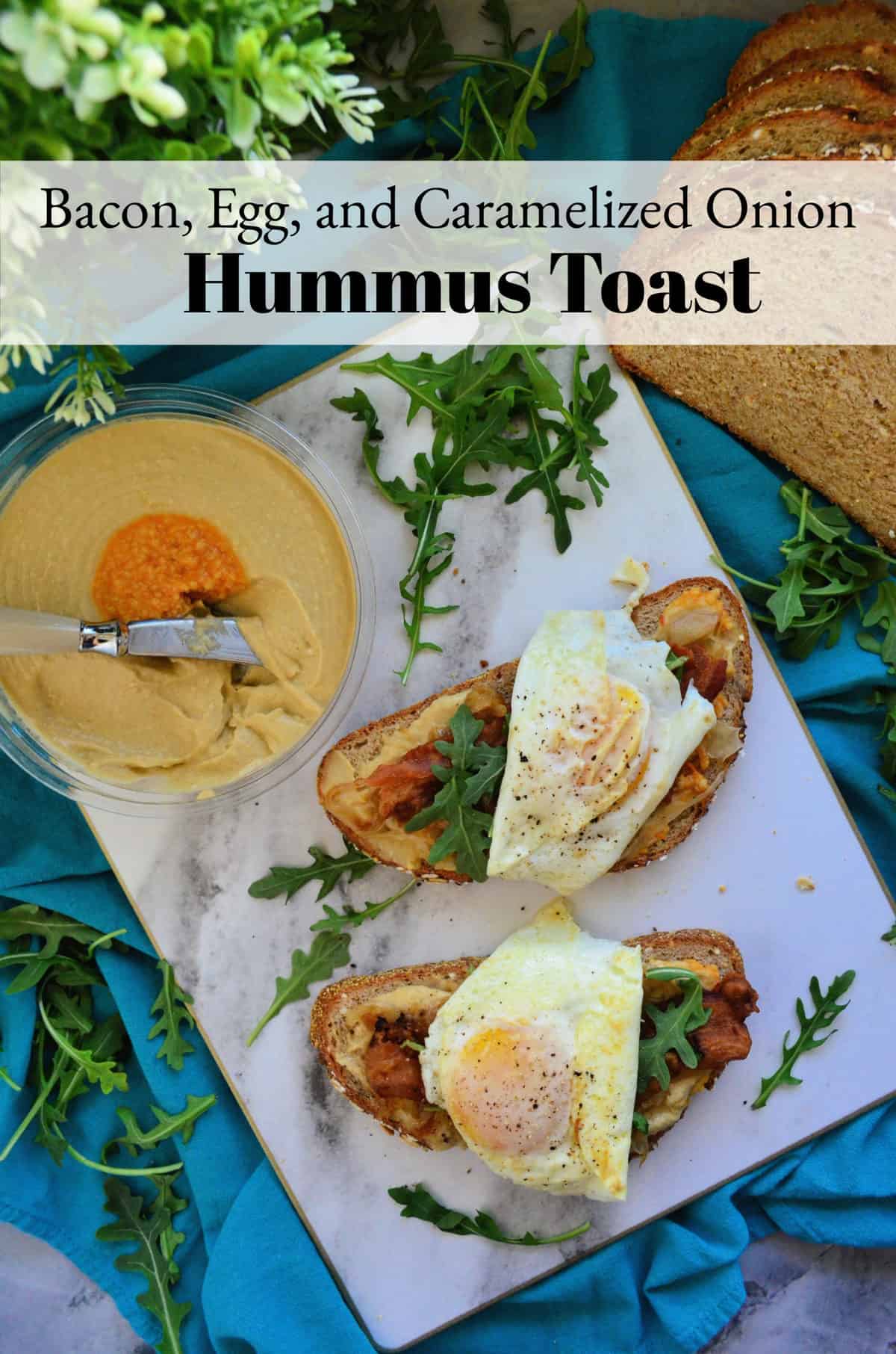 Hummus container, bread topped with hummus, bacon, eggs, arugula on platter with title text.