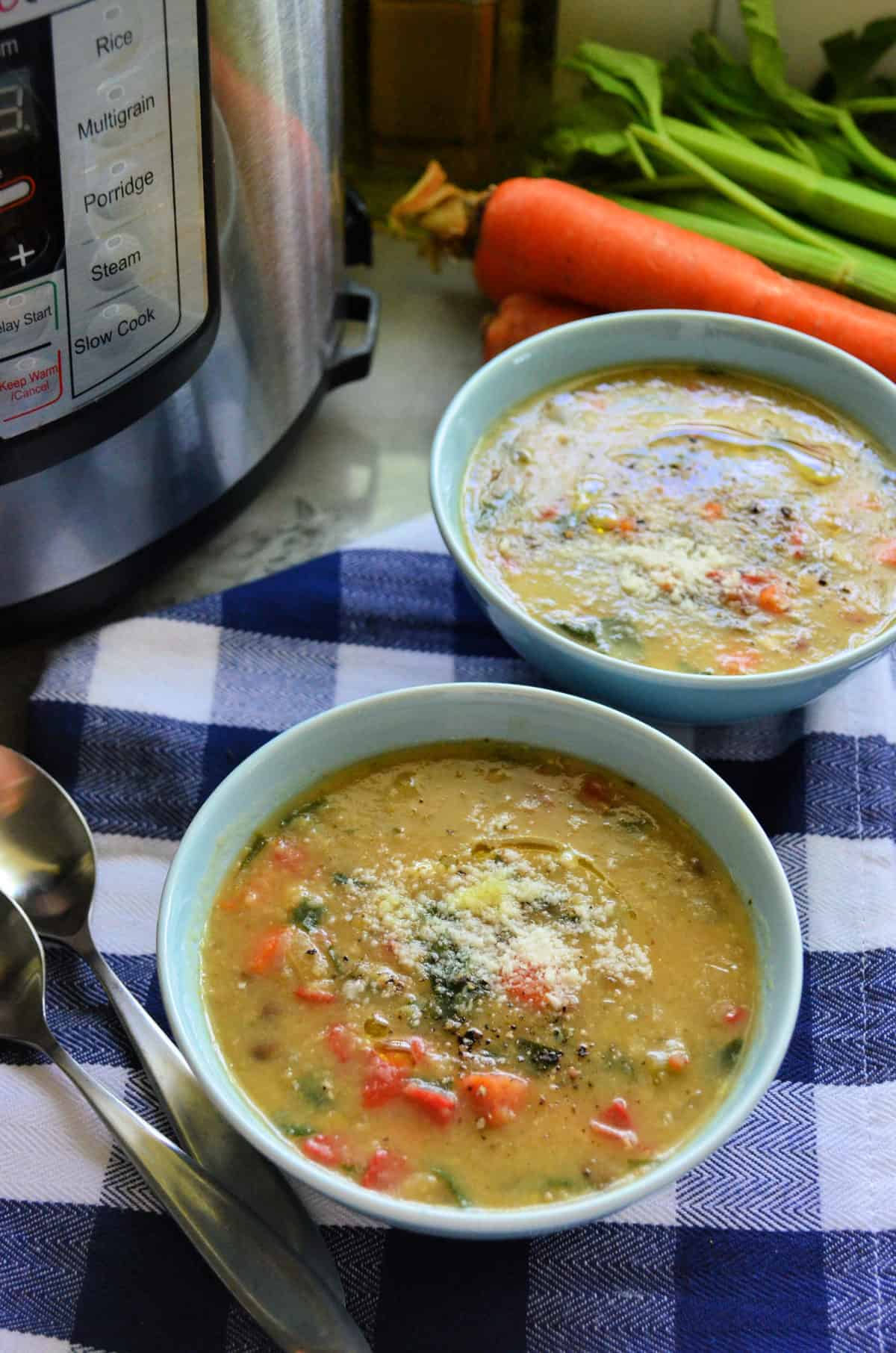 2 bowls of vegetable soup topped with parmesan cheese in front of instant pot, carrots, and celery.