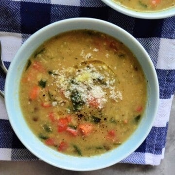 Top view of one bowl of yellowish soup with veggies and topped with parmesan cheese.