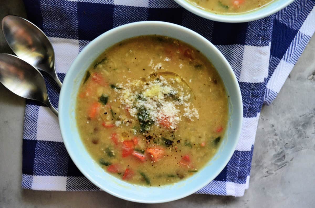 Top view of one bowl of yellowish soup with veggies and topped with parmesan cheese.