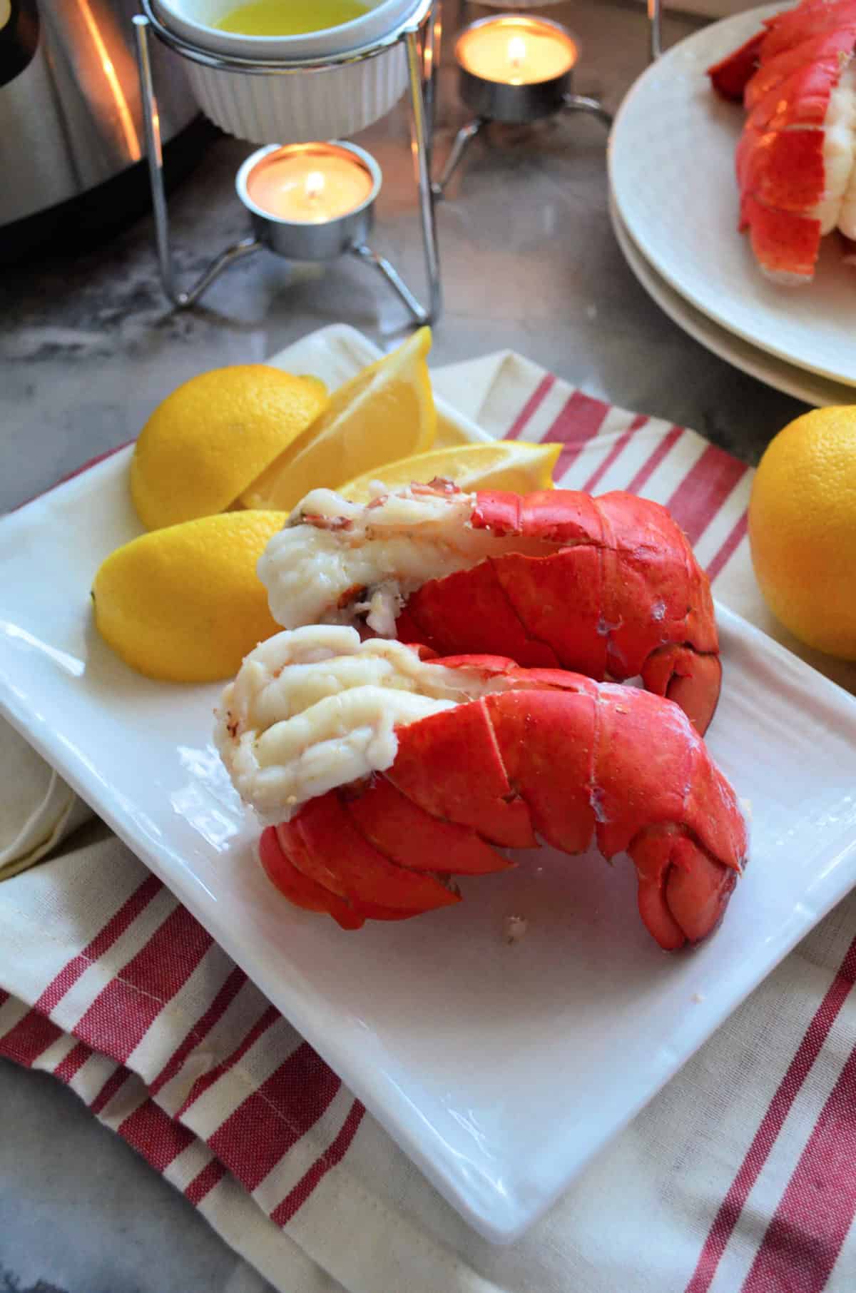 top view 2 plated lobster tails served with lemon wedges.