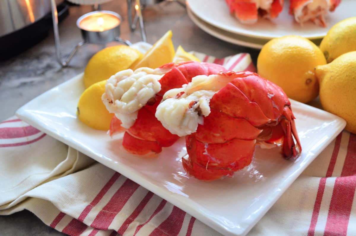 2 plated lobster tails served with lemon wedges.