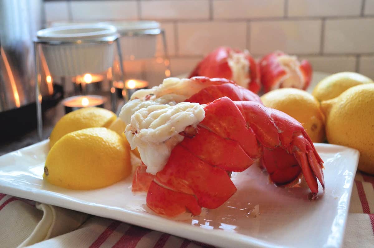 side of 2 plated lobster tails served with lemon wedges and butter.