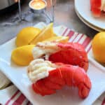 Two lobster tails on a white plate with lemon wedges.