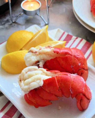 Two lobster tails on a white plate with lemon wedges.