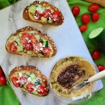 Top view of 3 bread slices topped with hummus, cucumber, tomatoes, and feta on board.