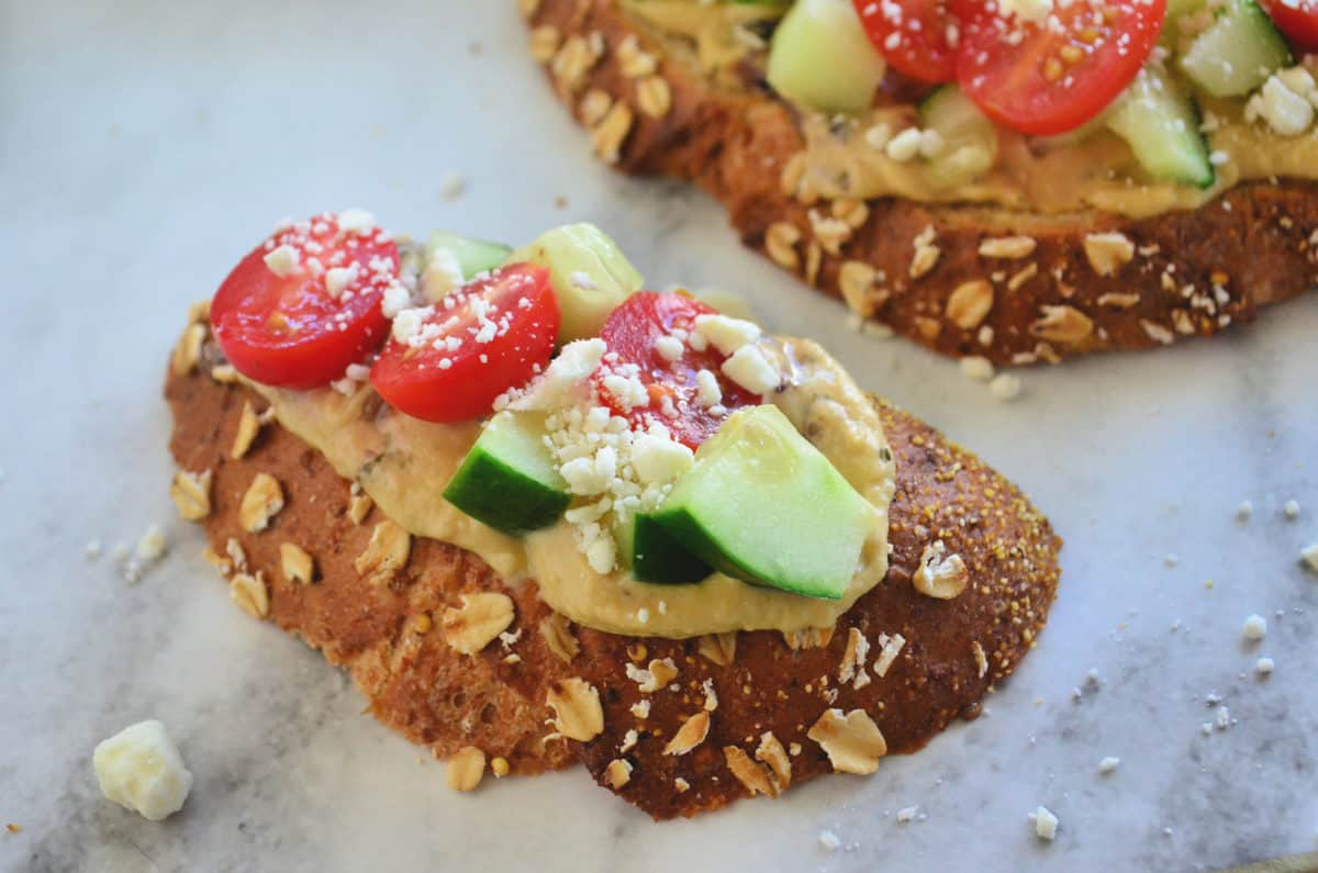 top view of toast slice topped with hummus, cucumber, tomato, and feta.