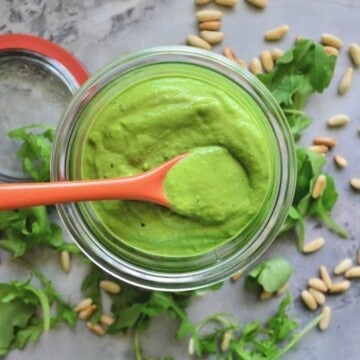 Top view of glass bowl full of thick green sauce with red spoon.