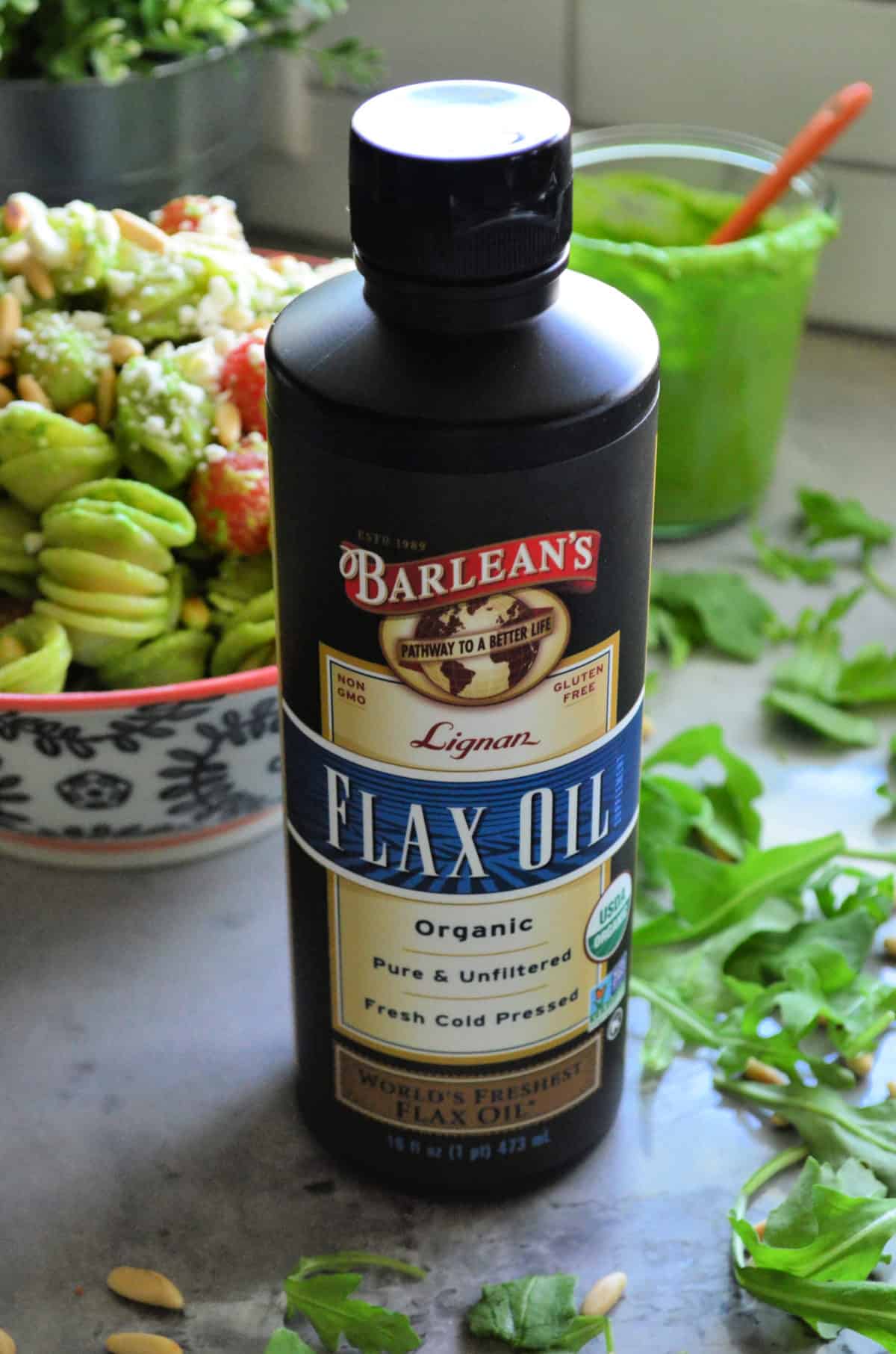 Close up bottle of Barlean's Flax Oil on countertop with pasta salad blurred in background.