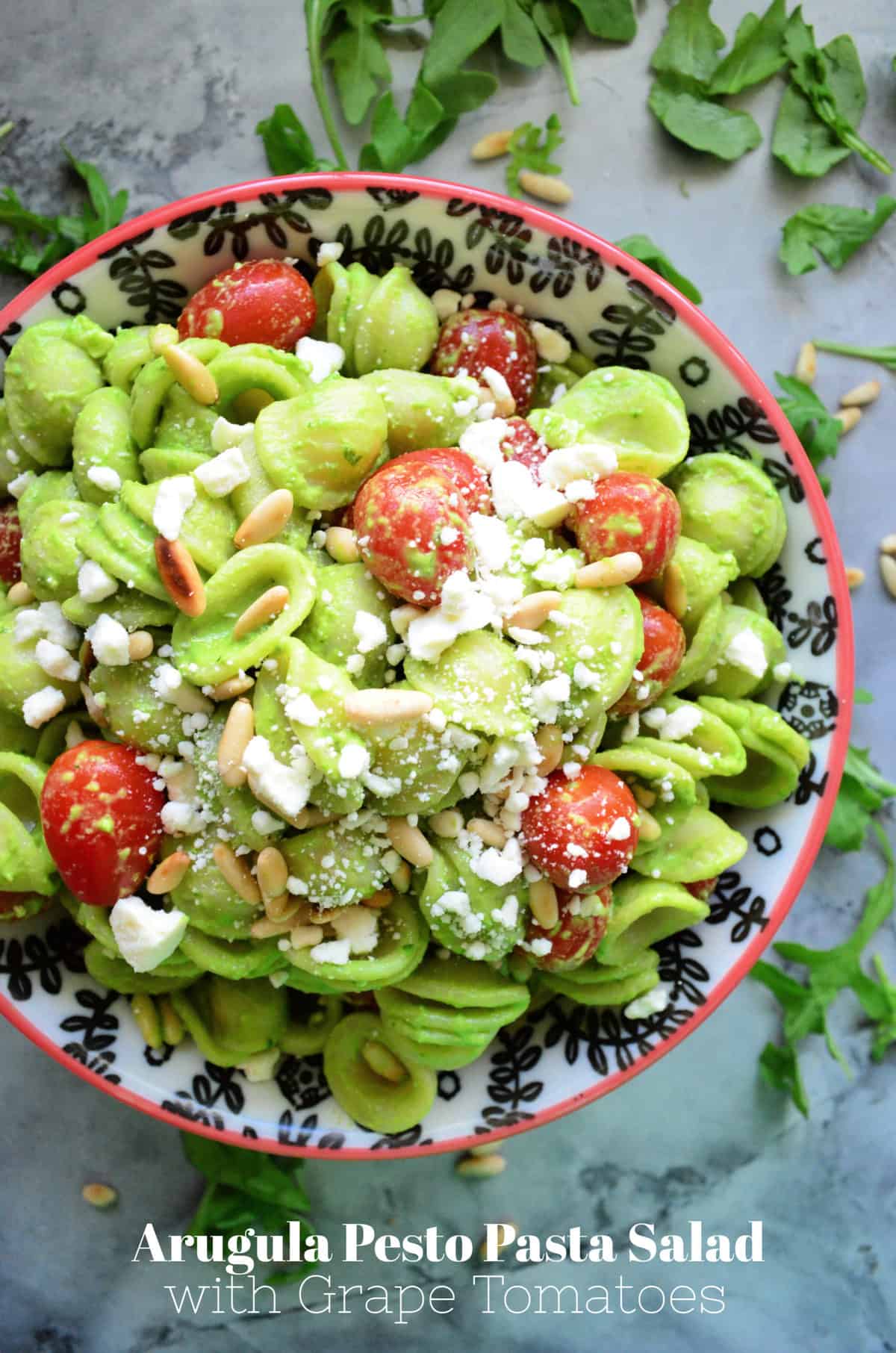 Bowl of orrichette pasta in green sauce with pine nuts, feta, grape tomatoes with title text.