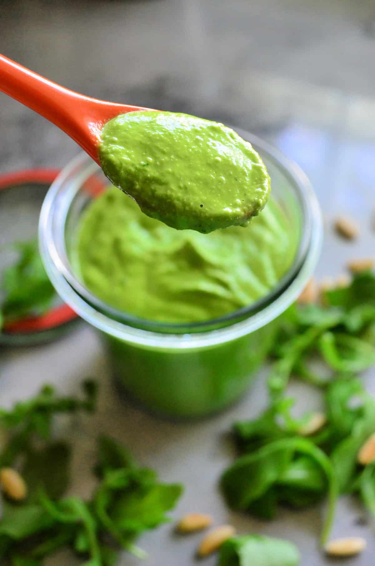 closeup spoonful of thick green sauce with glass bowl with thick green sauce blurred in background.