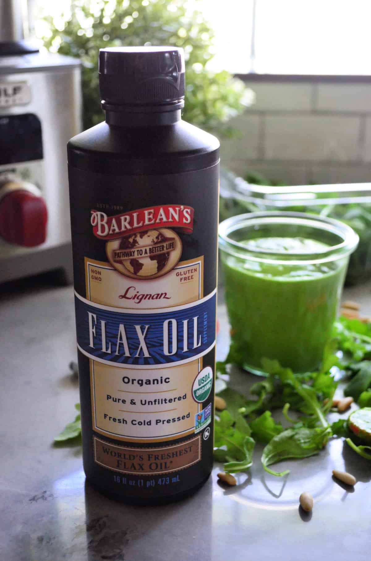 closeup bottle of Barlean's Flax Oil with glass of green sauce in background.